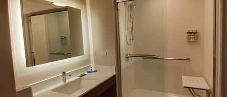 Un baño moderno con un espejo grande, un lavamanos, una ducha y un pequeño estante con artículos de tocador.