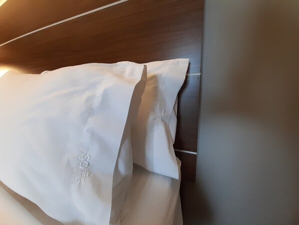 Almohada blanca con logotipo visible sobre un cabecero de madera.