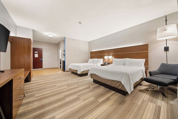 Quarto de hotel com duas camas, uma escrivaninha, uma cadeira, uma televisão e um abajur.