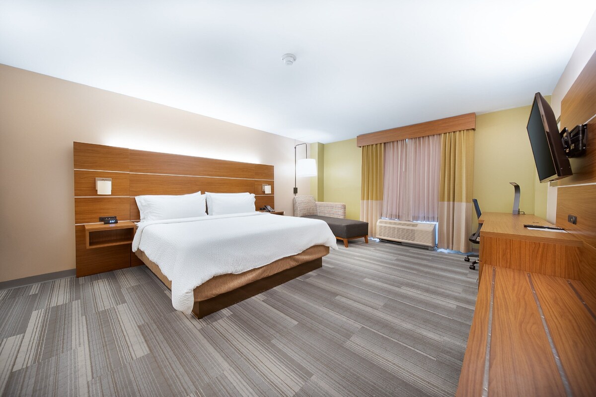 A hotel room with a large bed, a desk, a chair, a TV, and a window with curtains.
