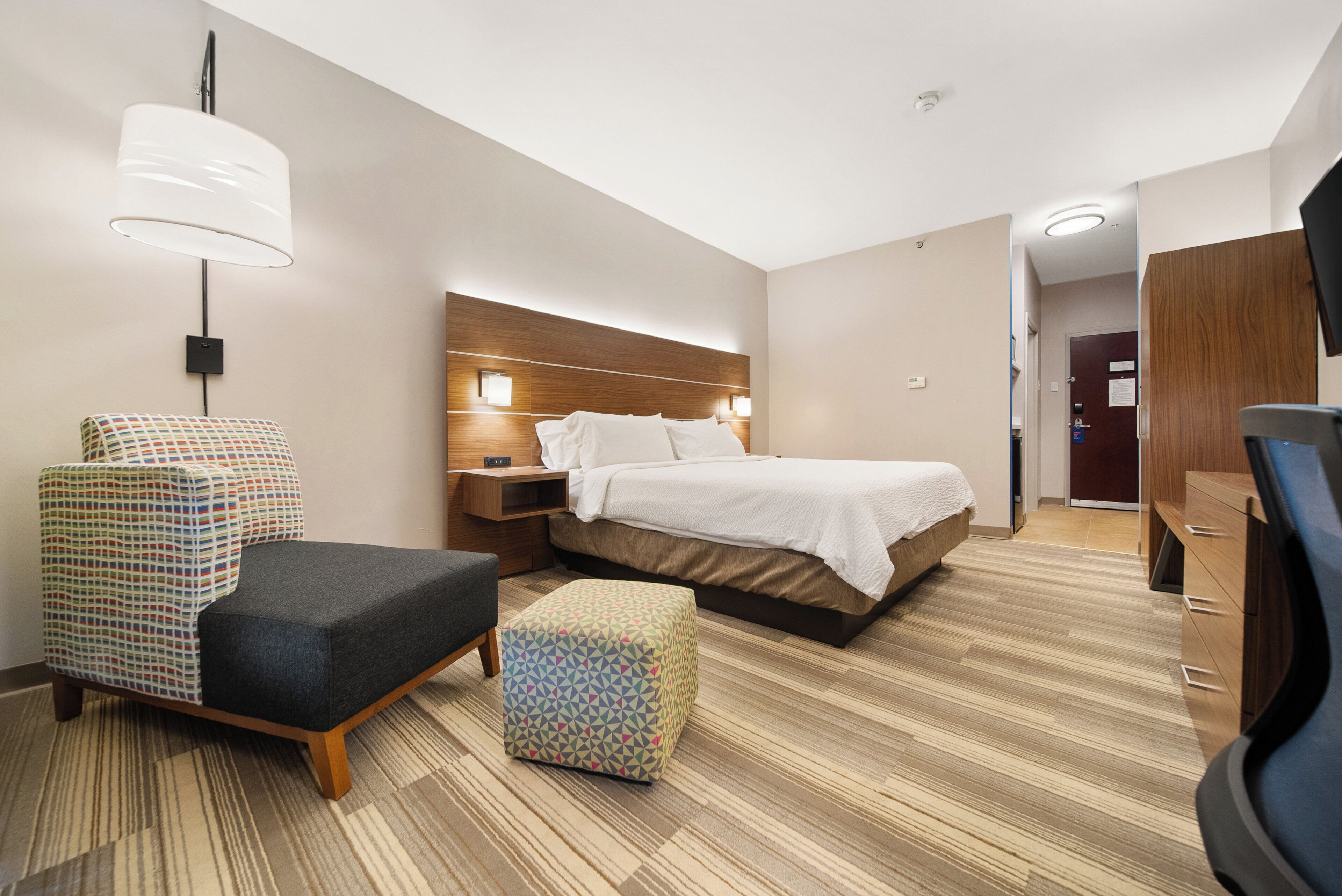 Een hotelkamer met een bed, een stoel, een klein tafeltje, een lamp en een kledingkast.