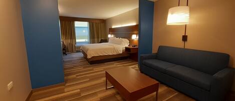 Una habitación de hotel con cama, sofá, mesa de centro y lámpara.