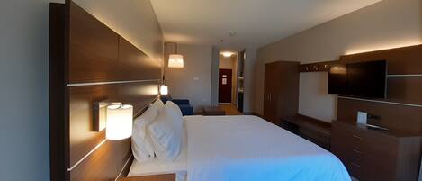 A hotel room with a large bed, bedside tables, a TV, and a wardrobe.