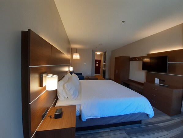 A hotel room with a large bed, bedside tables, a TV, and a wardrobe.