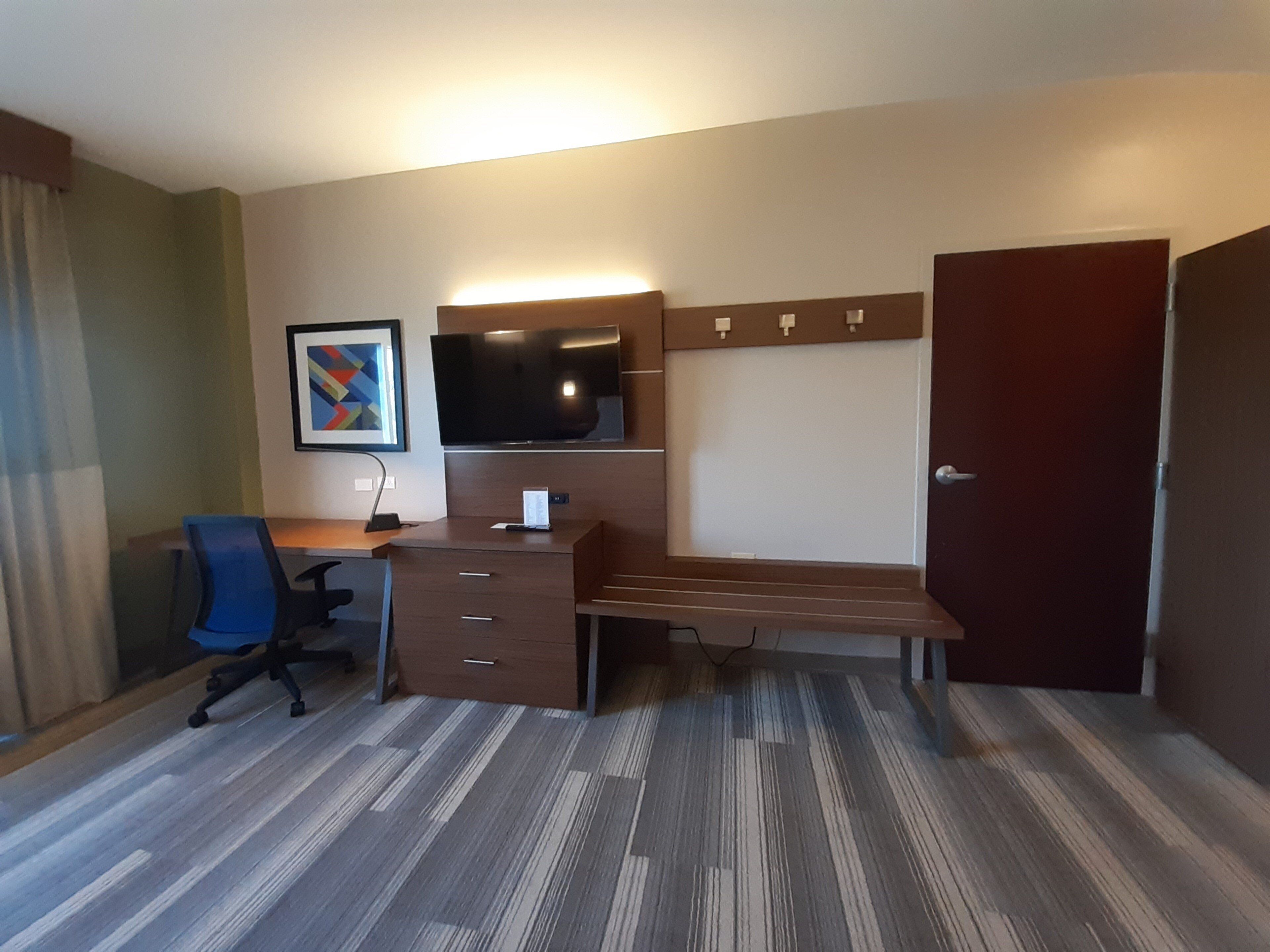 A hotel room with a desk, chair, television, and a door.
