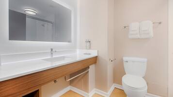 Een badkamer met een witte wastafel, spiegel en toilet, houten wastafelmeubel en een handdoekhouder.