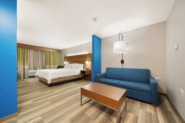 A hotel room with a bed, a sofa, a coffee table, a lamp, and a wall-mounted air conditioner. - Holiday Inn Express Hotel & Suites Trincity Trinidad Airport by IHG (Piarco)