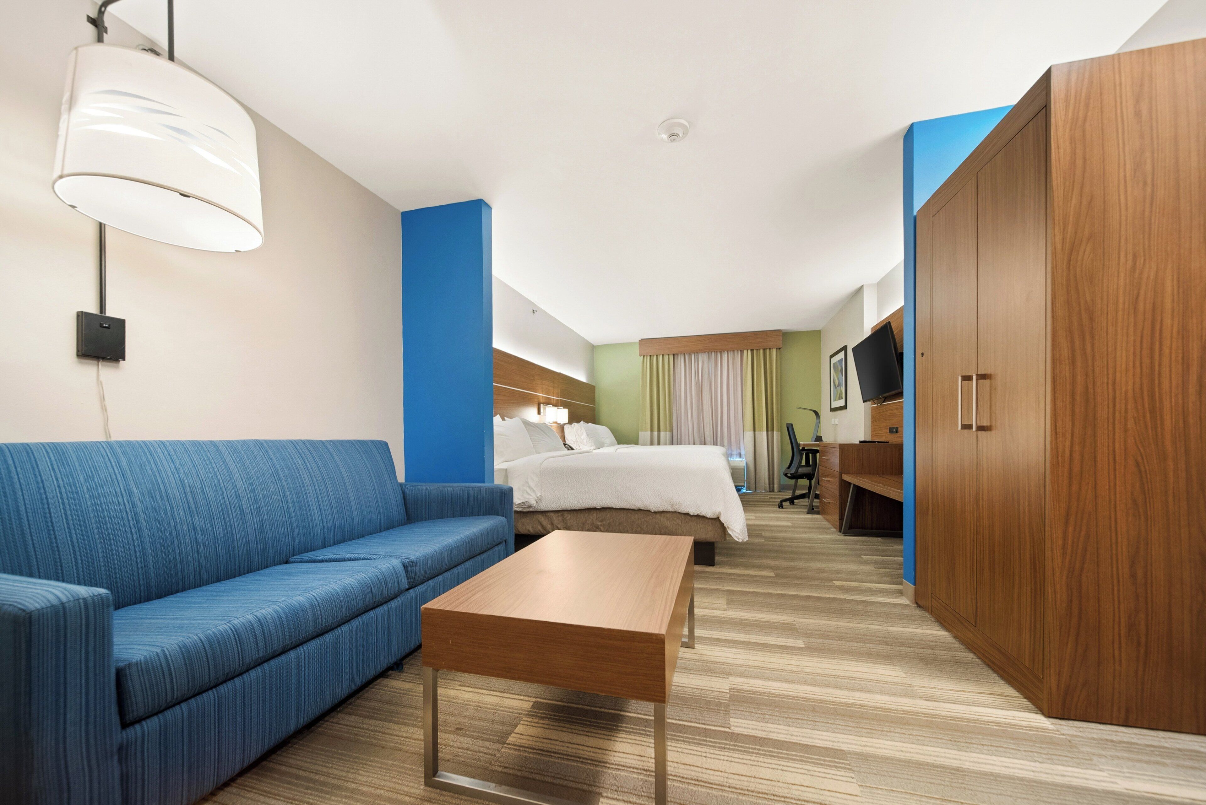 Una camera d'albergo con un divano blu, un tavolo in legno, un letto con biancheria bianca, una TV e un armadio.
