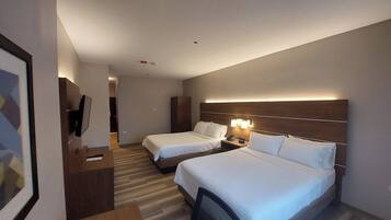 Habitación de hotel con dos camas, un escritorio, un televisor y cabecera con iluminación integrada.