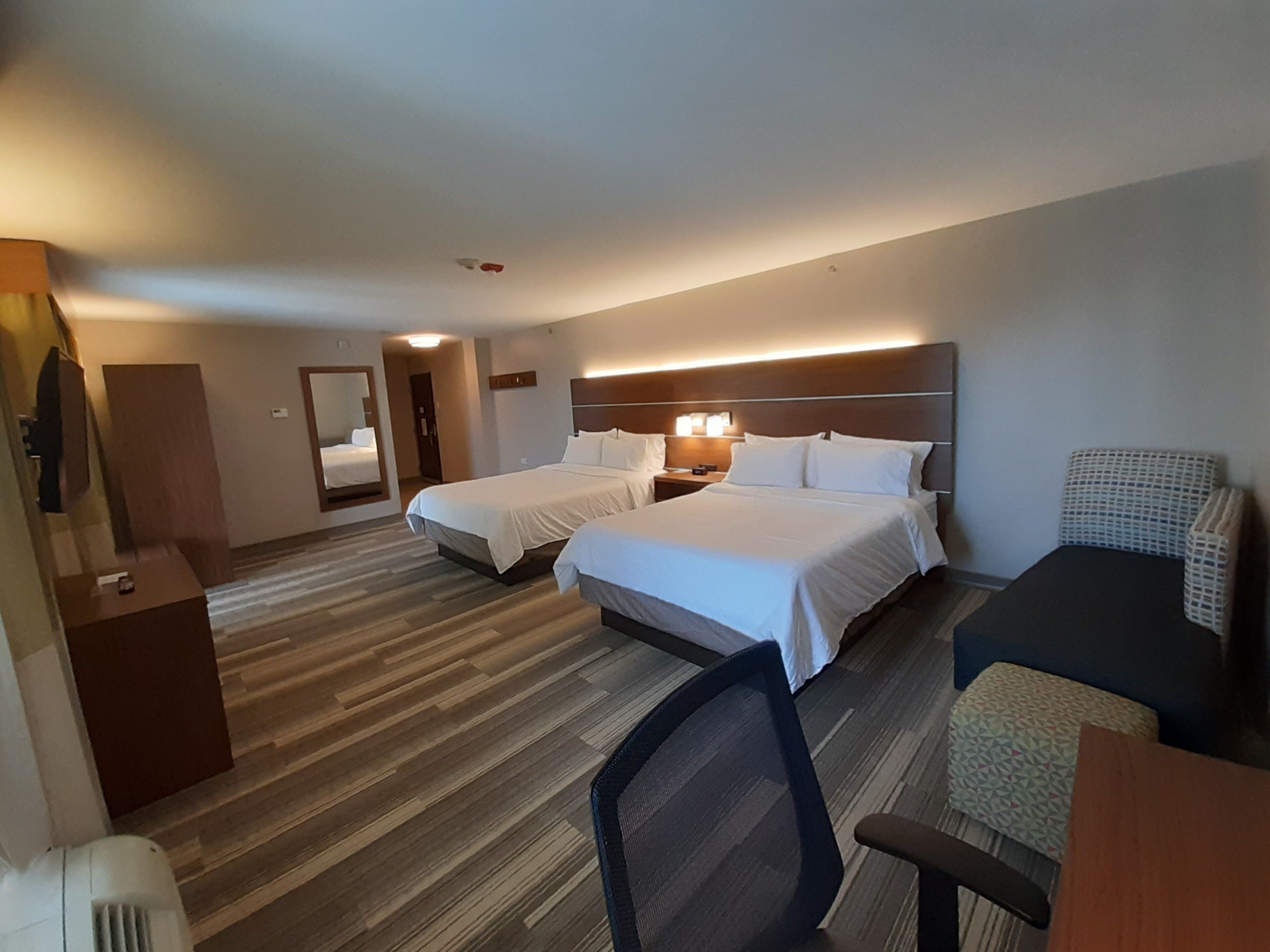 A hotel room with two beds, a desk, a chair, a mirror, and a wardrobe.