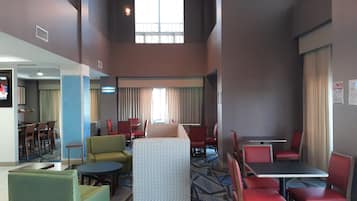 Un vestíbulo de hotel con varias zonas de estar, que incluyen un bar, un comedor y un salón con un sofá estampado.
