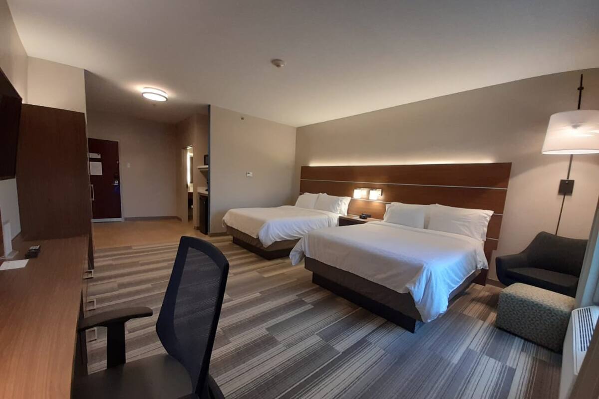 A hotel room with two beds, a desk, a chair, and a lamp.