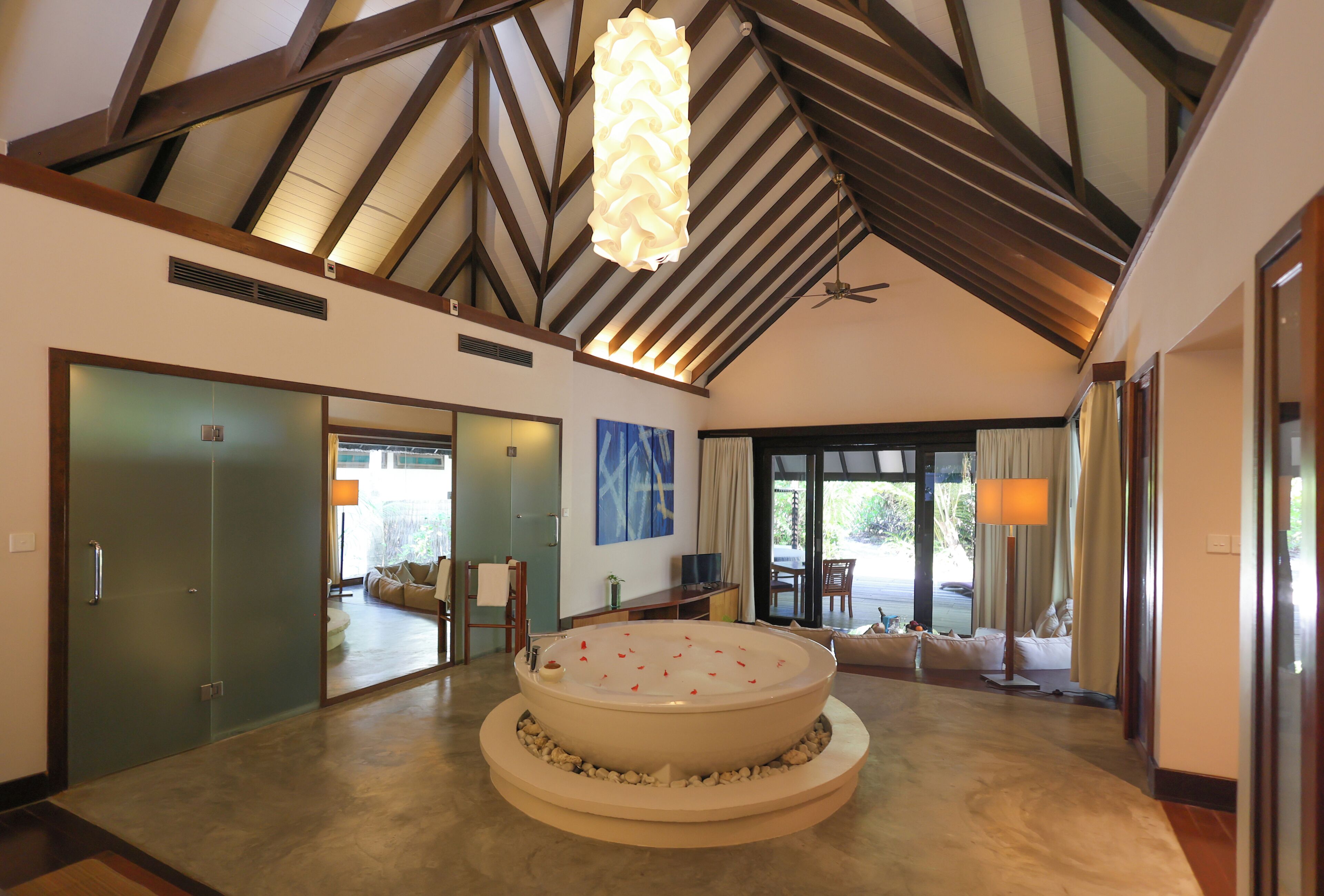 A spacious room with a large circular hot tub, a ceiling fan, and a view of the outdoors.