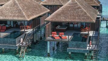 Bungalows sobre el agua con piscinas infinitas, techos de paja y aguas cristalinas azules.