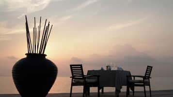 A dining table set for two with a large vase of sticks, overlooking a body of water.