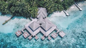 An overwater bungalows with multiple levels, connected by walkways, surrounded by clear turquoise waters and dense palm trees.