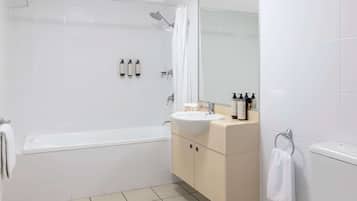 Un baño moderno con bañera, lavamanos e inodoro. Hay artículos de tocador en el lavamanos y una toalla colgada en el inodoro.