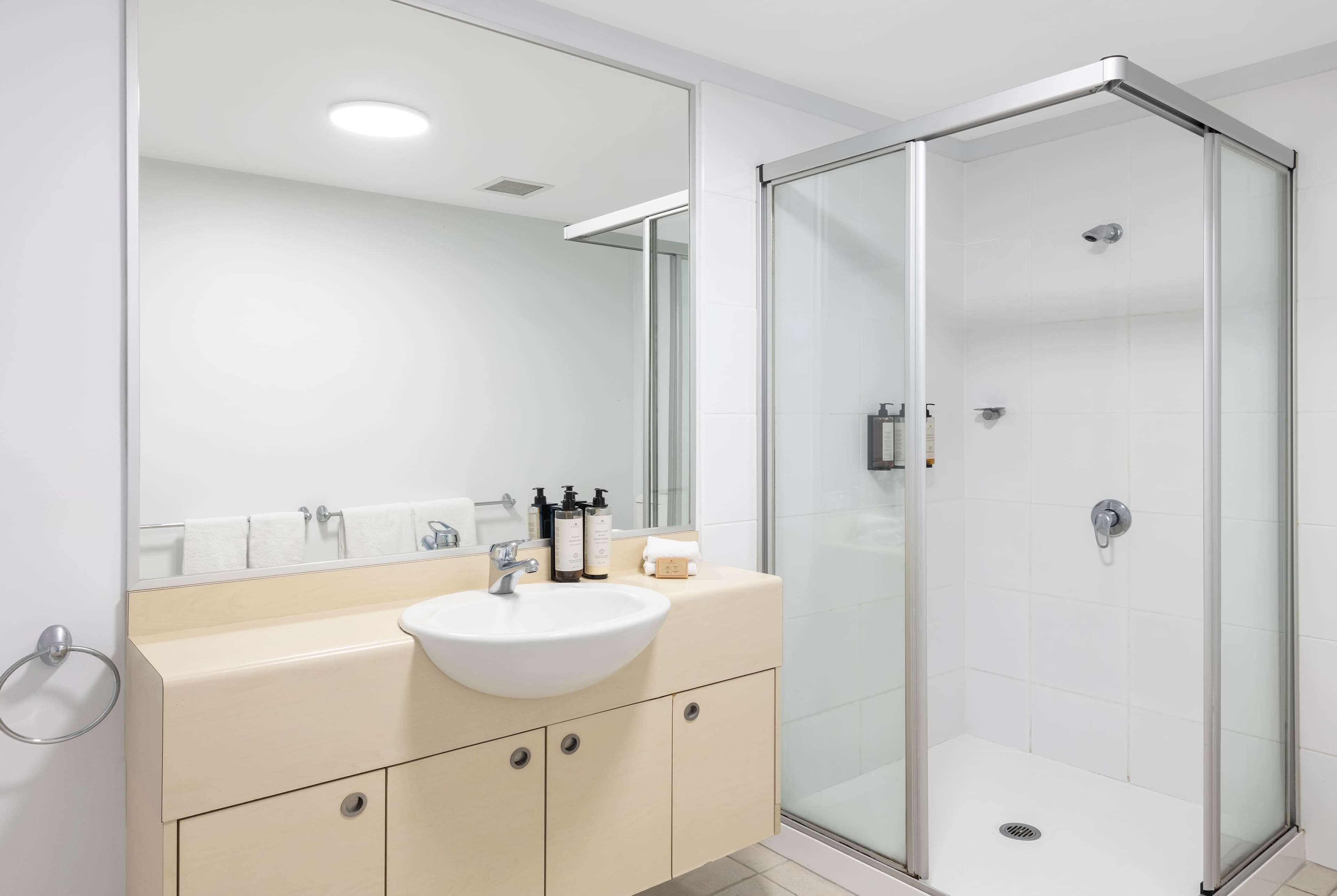 Een moderne badkamer met een wit wastafel, een beige badkamermeubel en een douche met glazen wanden.