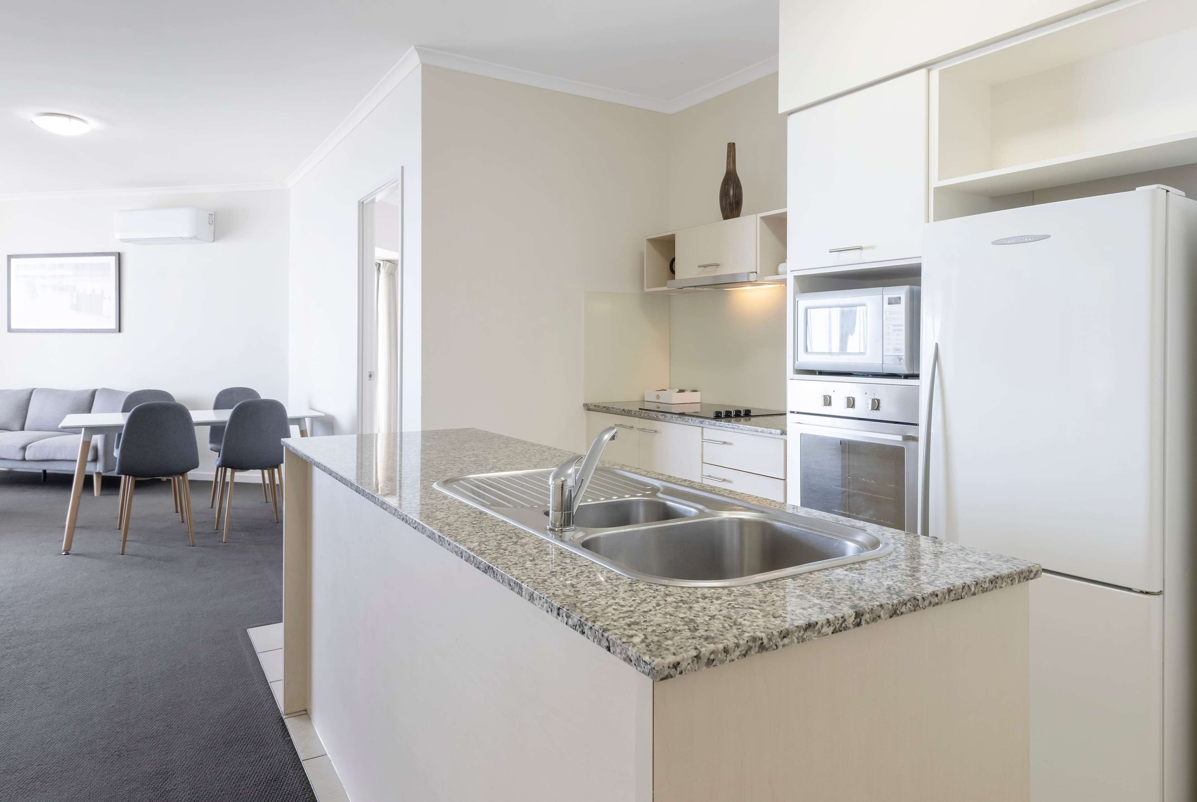 Una cocina moderna con encimera de granito, pileta de acero inoxidable y muebles color blanco.