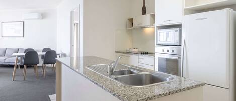 A modern kitchen with a granite countertop, stainless steel sink, and white cabinetry.