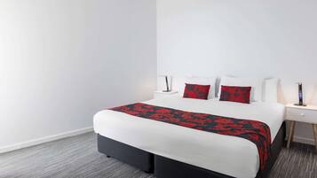 A hotel room with a large bed, white walls, and a grey carpet.