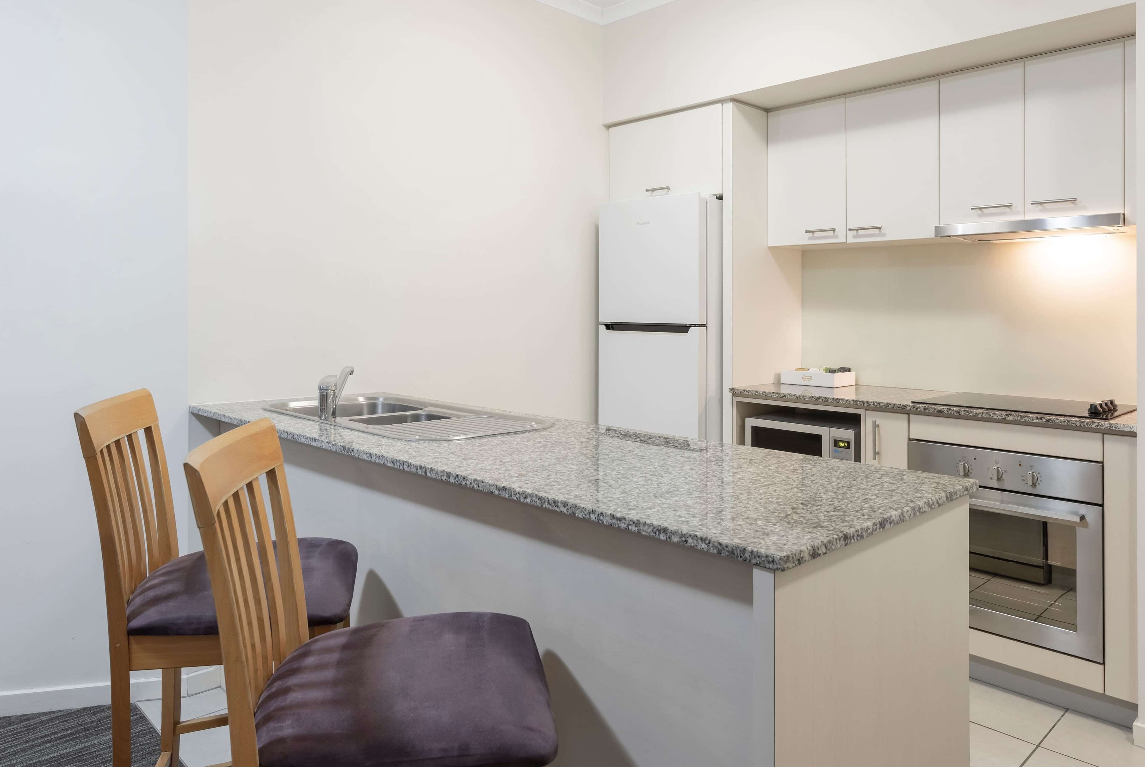Una cocina compacta con encimera de granito, horno integrado y muebles bajos blancos.