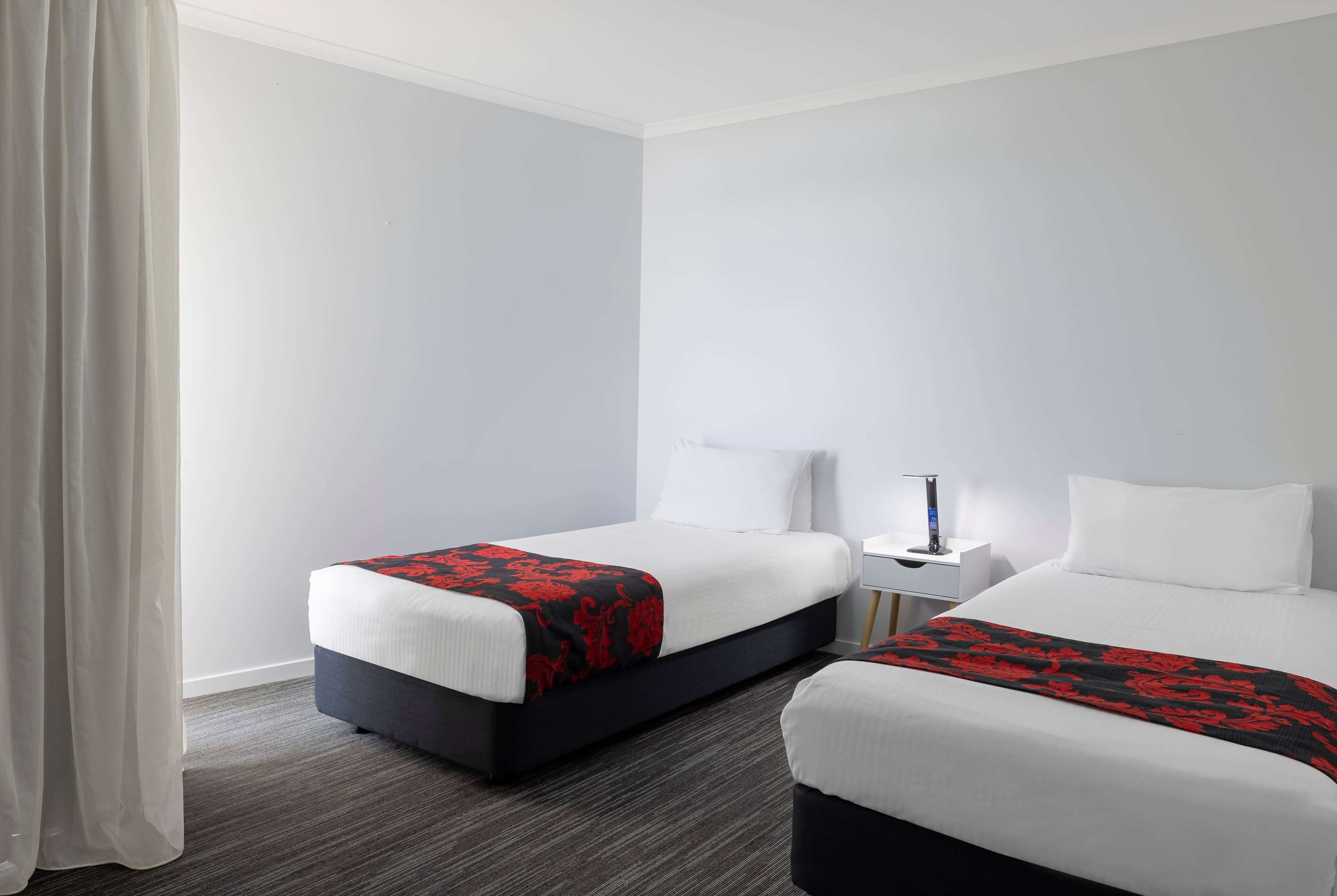 A hotel room with two beds, a nightstand, and a lamp.