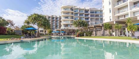 Un hotel con piscina, varios balcones y palmeras.