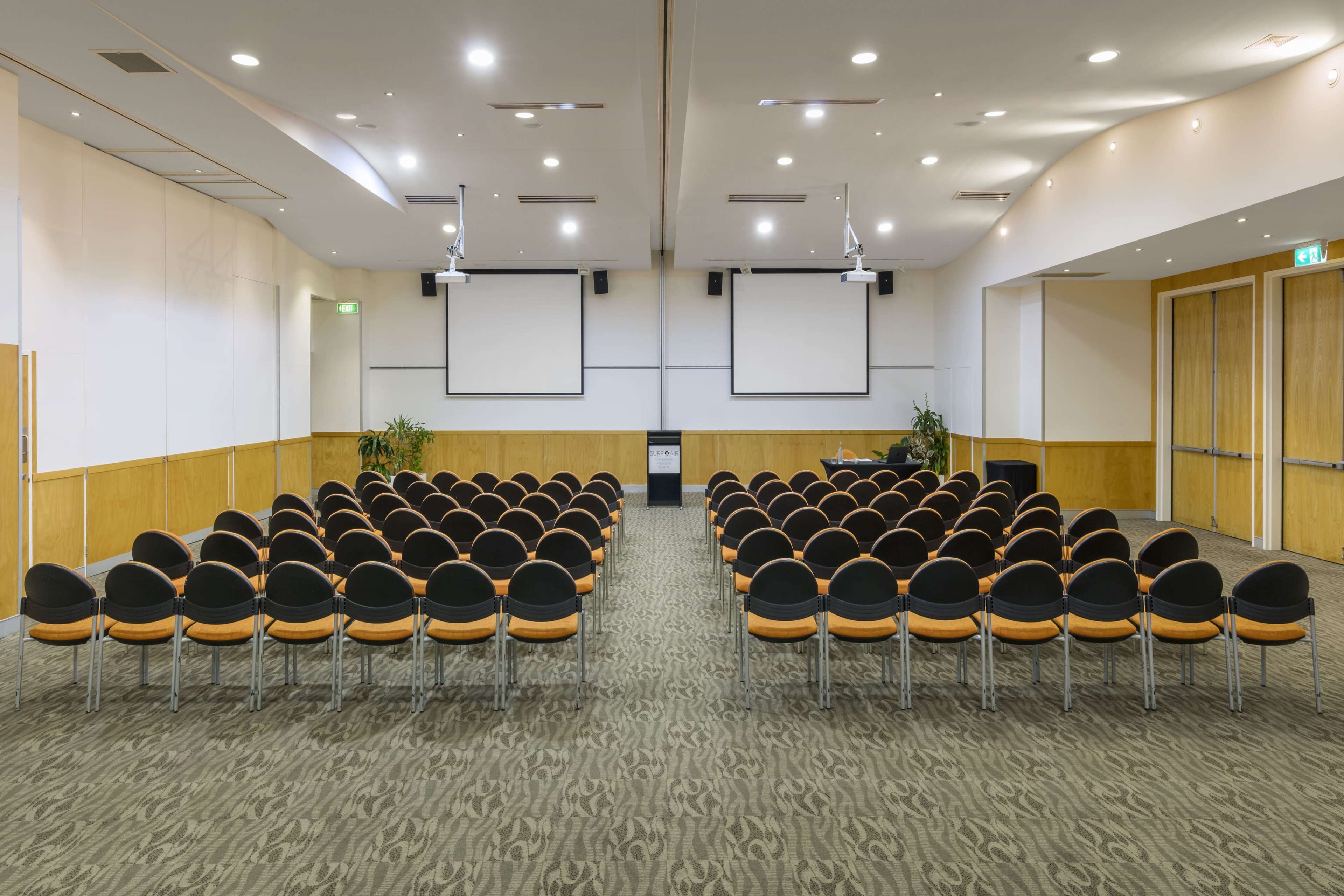 A conference room with rows of chairs, a projector screen, and a carpeted floor.
