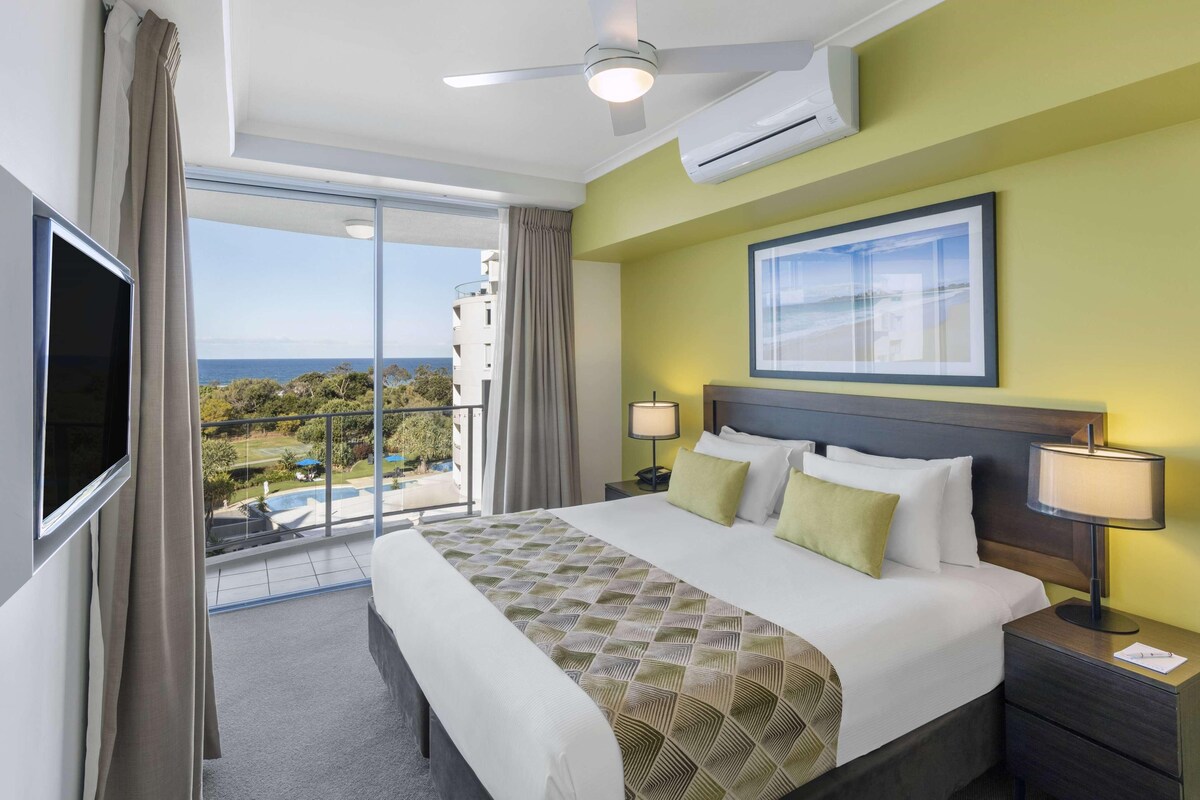 Habitación de hotel con una cama grande, televisor, balcón con vistas y aire acondicionado.