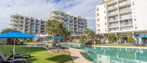 A hotel with a swimming pool, sun loungers, and umbrellas.