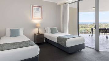 A hotel room with two beds, a nightstand, a lamp, and a large sliding glass door leading to an outdoor area with a view.