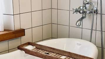 A white freestanding bathtub with a wooden tray, a shower head, and a hose.