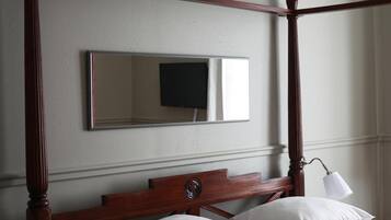 A four-poster bed with white bedding and a red throw blanket. A bedside table with a lamp and a book is visible.