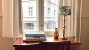 Een houten bureau met een stoel, een lamp en boeken bij een raam met gordijnen.
