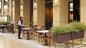 Una cafetería con mesas y sillas al aire libre, y una persona arreglando flores.
