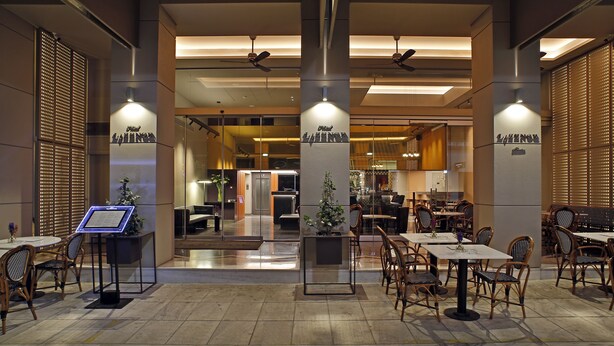 Un moderno vestíbulo de hotel con zonas de estar, un mostrador de recepción y una sección de restaurante a la vista.