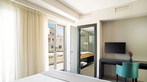 Habitación de hotel con cama, escritorio, silla, televisor y baño visible a través de una puerta abierta.