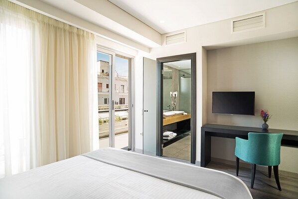 Habitación de hotel con cama, escritorio, silla, televisor y baño visible a través de una puerta abierta.