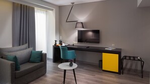 Una sala de estar moderna con un sofá, una mesita redonda, una silla azul, un televisor y un escritorio con un armario amarillo.