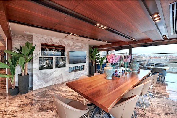 A modern dining area with a wooden table, chairs, and large potted plants.
