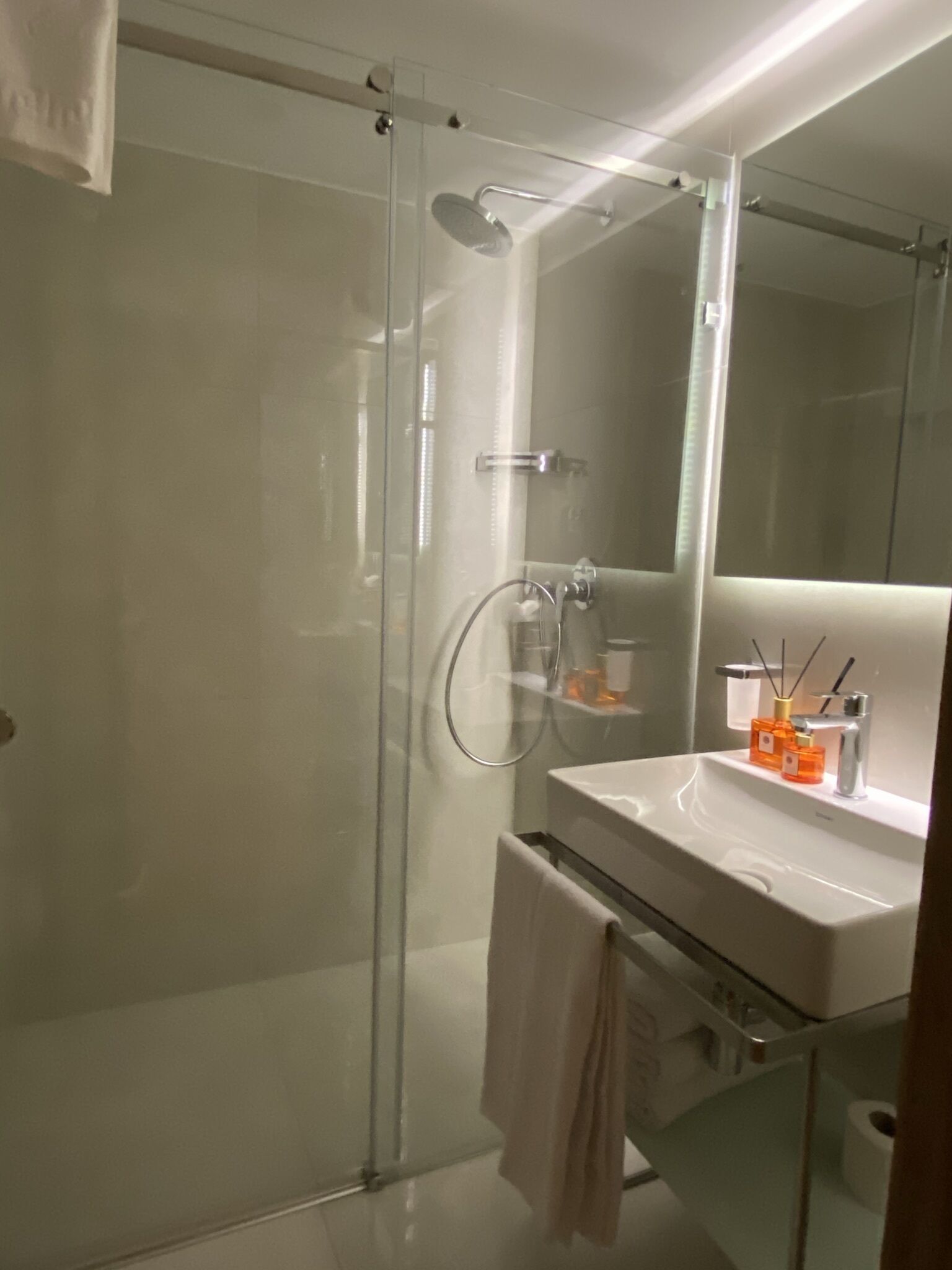 A modern bathroom with a glass-enclosed shower, a white sink with a mirror, and a towel hanging on a rack.
