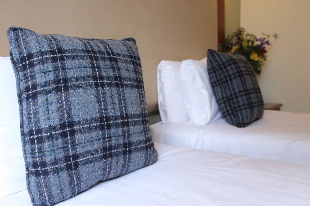Une chambre d’hôtel avec deux lits, chacun doté de draps blancs et d’un oreiller à motifs écossais.