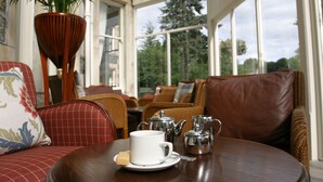 A conservatory with wicker furniture, a white cup, and silver teapots on a table. - Craiglynne Hotel (Grantown-on-Spey)
