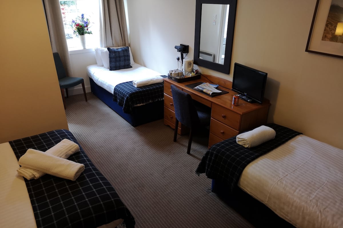 Une chambre d’hôtel avec deux lits, un bureau avec un ordinateur, une chaise et une fenêtre avec des rideaux.