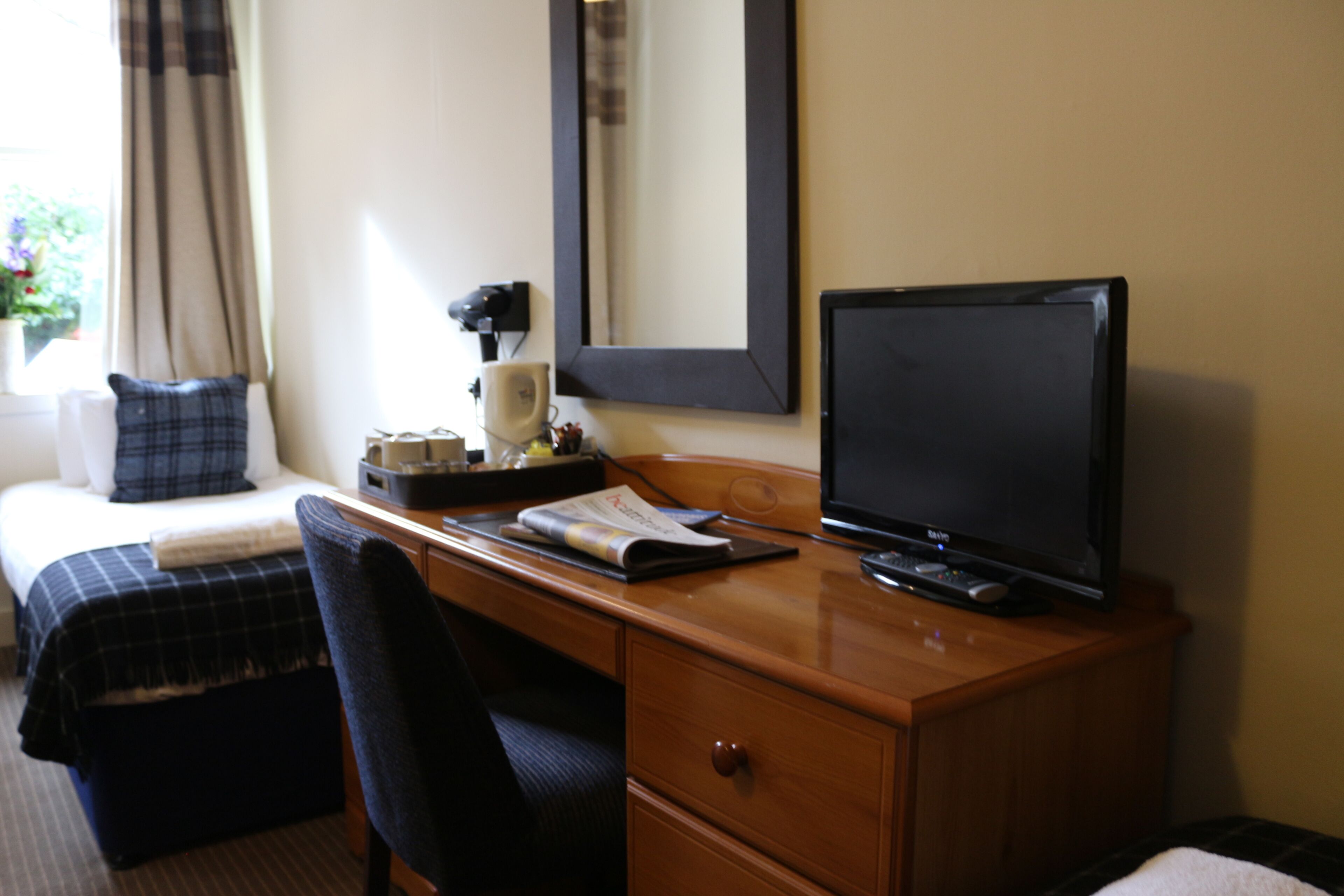 A hotel room with a bed, a desk with a computer, a chair, and a mirror.