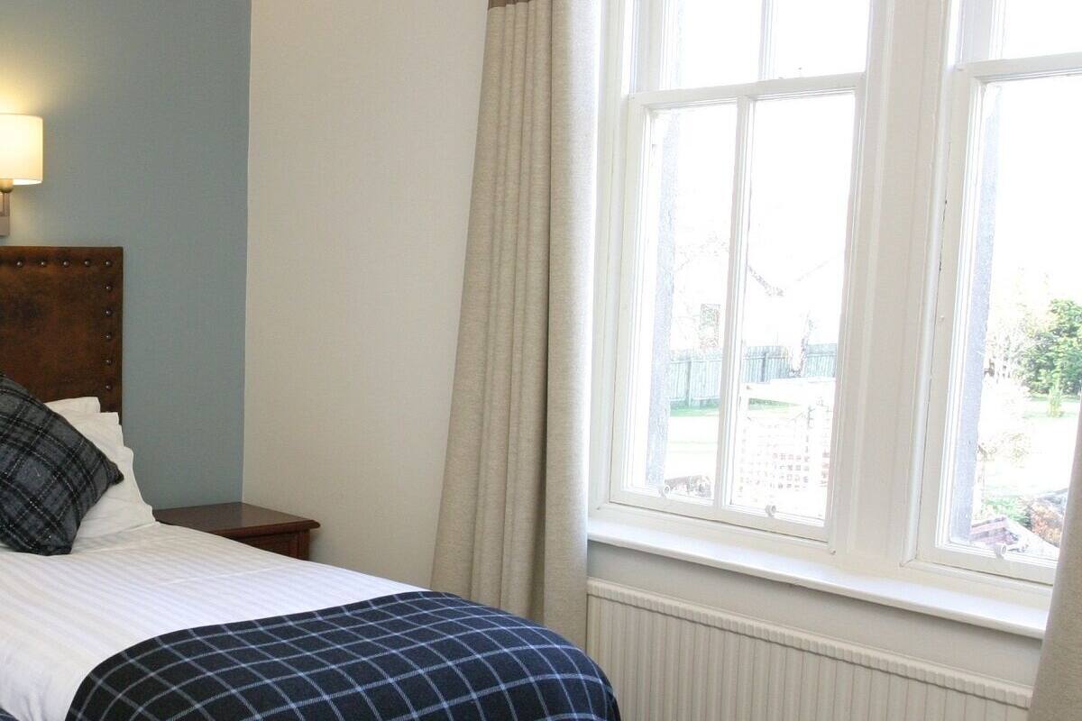 Un dormitorio con cama, mesita de noche, lámpara y ventana con cortinas.