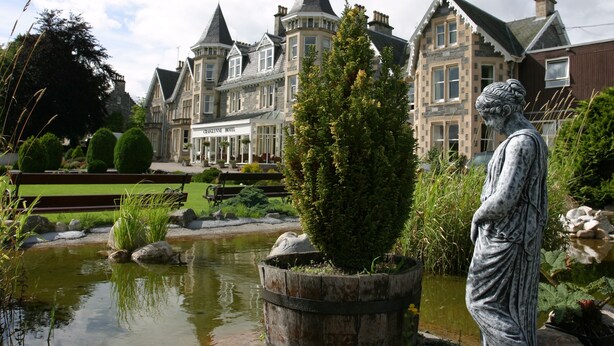 A historic building with a statue in the foreground, a pond, and a well-maintained garden. - Craiglynne Hotel (Grantown-on-Spey)