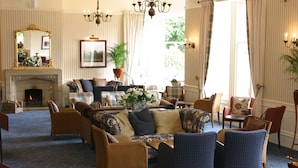 A spacious living room with a fireplace, comfortable seating, and large windows. - Craiglynne Hotel (Grantown-on-Spey)