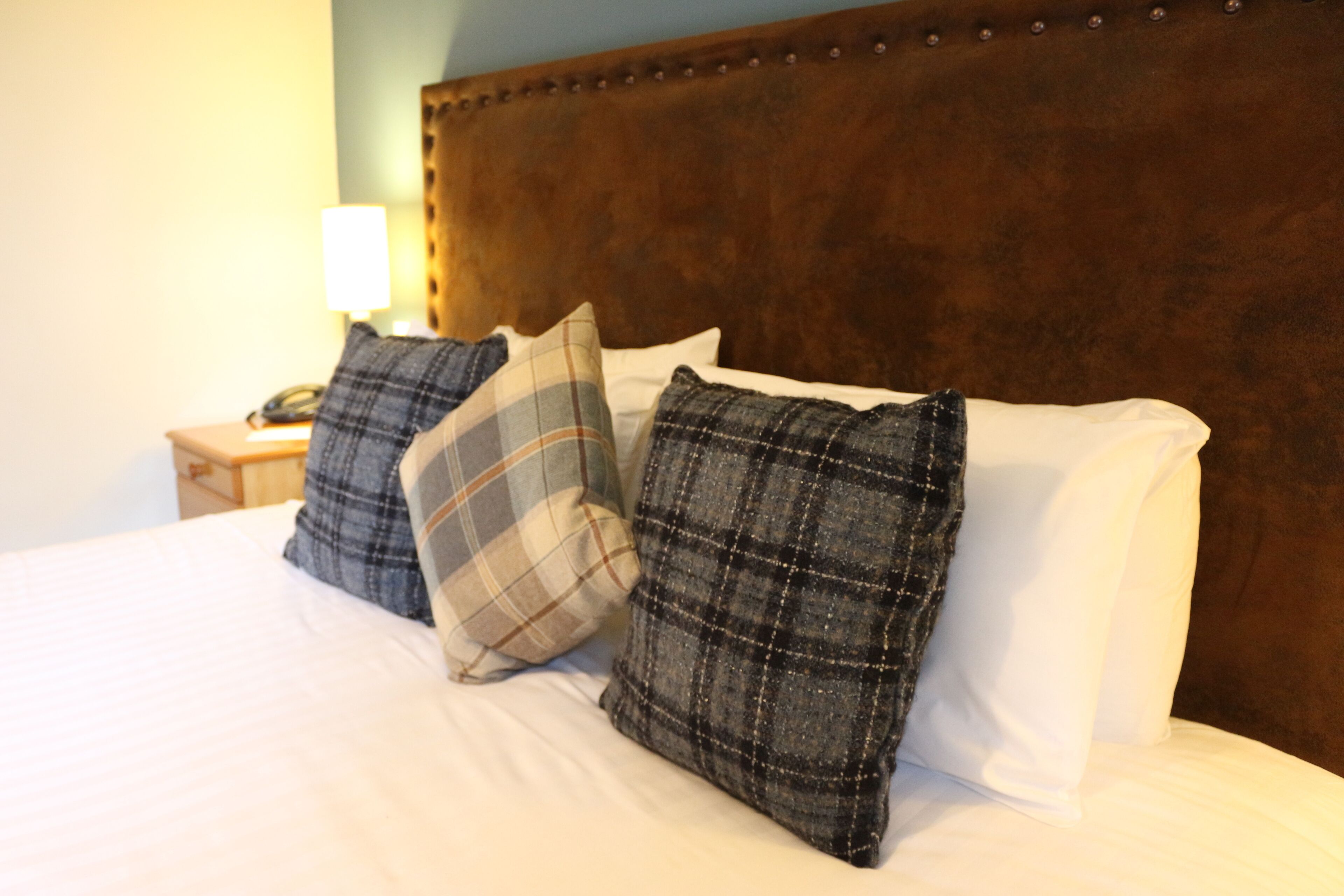 A bed with white sheets and three plaid pillows.